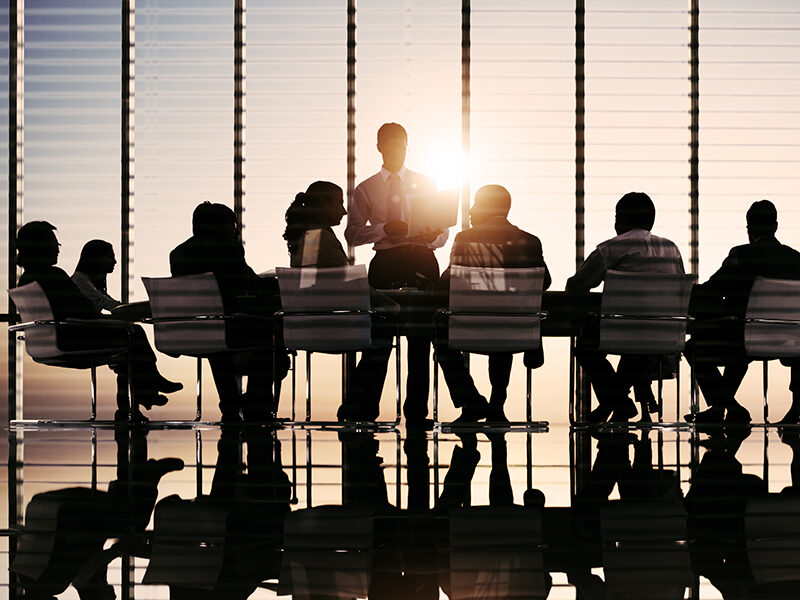 Board directors assemble in a meeting room, silhouetted by the sunshine